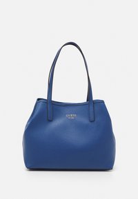 Niebieska skórzana torba na ramię marki Guess z podwójnymi ramiączkami i srebrnym logo marki umieszczonym na środku z przodu.