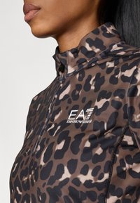Blusa de mangas compridas com padrão de leopardo, em tons de castanho e preto, com gola alta e fecho de zipper. Apresenta o logótipo da marca "EA7 Emporio Armani" no peito.