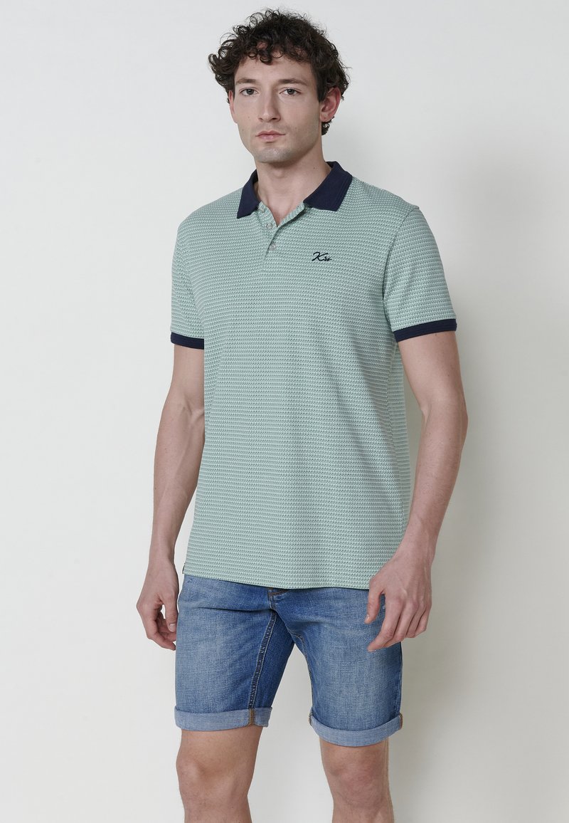 Světle zelené textured polo tričko s námořnickým límcem a manžetami, zdobené malým vyšívaným logem. V kombinaci s zkrácenými džíny.