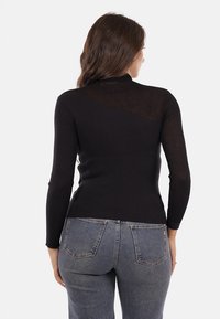 Top lungo a maniche nere con costine, caratterizzato da un collo alto e un dettaglio con apertura sulla schiena, abbinato a jeans in denim blu a vita alta.