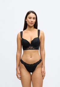 Czarny koronkowy biustonosz typu bralette z formowanymi miseczkami, przezroczystymi detalami, regulowanymi cienkimi ramiączkami oraz dopasowane koronkowe stringi z ząbkowanymi krawędziami.