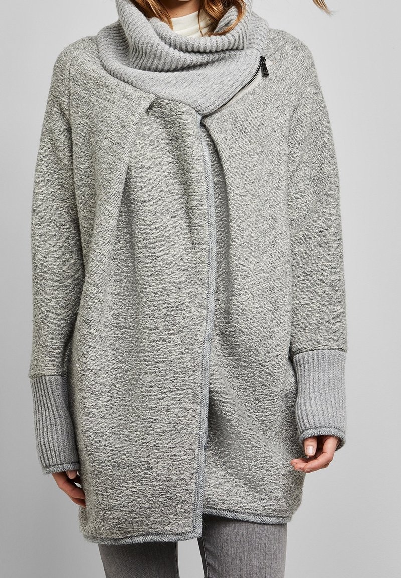 Grå oversize tröjcoat med cowl-neck, tillverkad av textilier med struktur, med ribbade ärmar och dragkedjestängning på ena sidan.