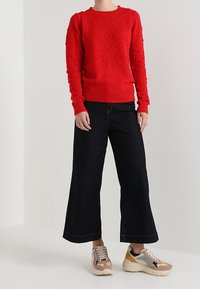 Pull rouge en maille avec motifs de cœurs, assorti à un jean large foncé et des baskets multicolores. Tissu décontracté et texturé.
