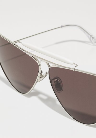 Ochelari de soare aviator din metal cu lentile negre, cadru argintiu, accente albe pe punte și suporturi de nas ajustabile.
