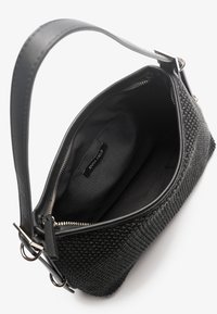 Černá tkaná kabelka s texturovaným tělem, hladkými černými koženými detaily a stříbrným kováním. Otevřený vršek odhaluje jednoduchý černý vnitřek.