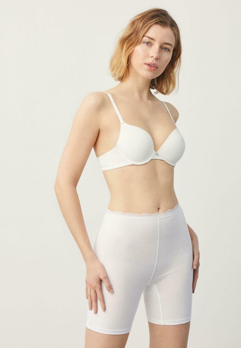 Sujeta de blanco con copas lisas y tirantes ajustables, combinada con pantalones cortos blancos que tienen un dobladillo de encaje en la cintura y una tela suave y elástica.