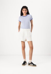 Chemise à rayures bleues et blanches à manches courtes, shorts blancs à taille élastique et baskets noires avec rayures blanches, se tenant sur un fond blanc.