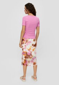 Różowa, prążkowana bluzka z krótkim rękawem i falbaniastymi brzegami zestawiona z długą spódnicą w tie-dye w odcieniach różu, brązu i niebieskiego. Całość dopełniają casualowe obuwie.