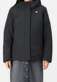 Černá zateplená bunda s předním zipem, kapucí a bočními kapsami. Na hrudi je malá nášivka. Hladká textura a moderní design.