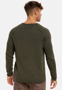 Chemise à manches longues vert foncé avec un motif texturé en côtes et des manches raglan. Détails de couture visibles le long des épaules et de l'ourlet.