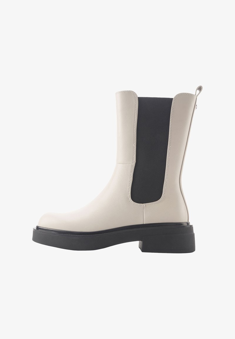 Bottine en cuir beige avec panneau élastique noir, bout rond et semelle épaisse noire. Dispose d'une languette pour un enfilage facile.