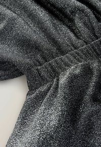 Textil negru strălucitor cu o suprafață texturată și un sclipici subtil, având detalii plisate de-a lungul marginilor și o cădere netedă.