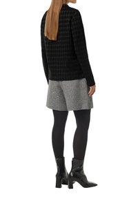 Czarny sweter w wzór houndstooth, szare szorty w wzór houndstooth, czarne rajstopy, czarne botki na wysokim obcasie do kolan; modelka odwrócona tyłem, widoczne długie brązowe włosy.