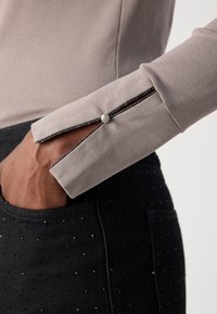 T-shirt à manches longues en jersey gris clair avec un détail de manche fendue, rehaussé d'une bordure noire et d'un bouton blanc, associé à un pantalon noir à pois.