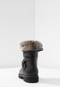 Botte en cuir noir avec un bout rond, un col en fourrure grise pelucheuse et un détail de boucle sur le côté. Semelle texturée pour adhérence et stabilité.