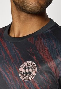 Maillot de sport noir avec des rayures diagonales rouges et bleues, arborant un logo circulaire du FC Bayern München sur la poitrine, design à col rond.