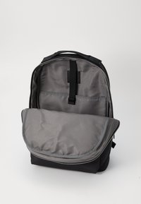 Mochila negra con un interior gris. Cuenta con un cierre con cremallera, una solapa frontal y bolsillos internos para una mejor organización. Textura suave.