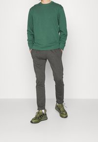 Chemise en coton verte à manches longues, pantalon gris fuselé et baskets vertes avec des accents noirs. Le pantalon a une ceinture élastique pour le confort.