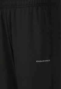 Svarta atletiska shorts tillverkade av glatt tyg har en elastisk midja och en reflektiv "ENDURANCE"-logotyp på det nedre benet.