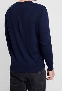 Marinblå tröja med ribbade muddars och nederkant, med rund halsringning och en mjuk, stickad textur. Synlig sömnad på axlarna.