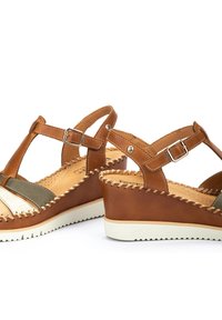Sandales compensées en cuir marron avec un design en T, présentant des accents verts et métalliques, des détails cousus et une semelle extérieure blanche texturée.