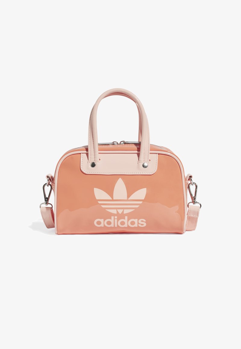 Růžová lakovaná kožená kabelka s dvojitými uchy a odnímatelným popruhem na rameno. Na přední straně se nachází velké bílé logo Adidas a stříbrné kovové doplňky.