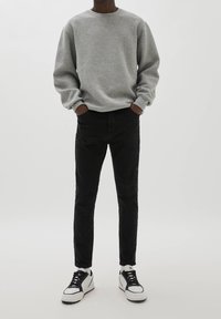 Sudadera gris de manga larga, combinada con jeans negros ajustados y zapatillas blancas con cordones negros. Conjunto sencillo y casual.