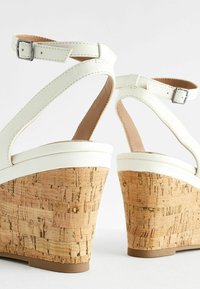 Des sandales compensées blanches en cuir présentent une plateforme en liège au fini texturé, des brides de cheville réglables et un bout lisse et arrondi.