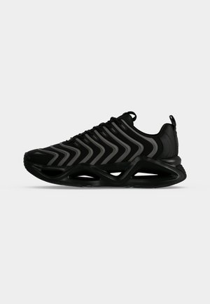 Baskets noires de sport avec des rayures grises ondulées, une semelle intermédiaire géométrique creuse unique, et une languette au talon sur fond blanc.