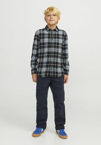 Camisa de cuadros en blanco y negro con acentos azules, combinada con pantalones cargo color marino y zapatillas azules con suelas de goma marrón.