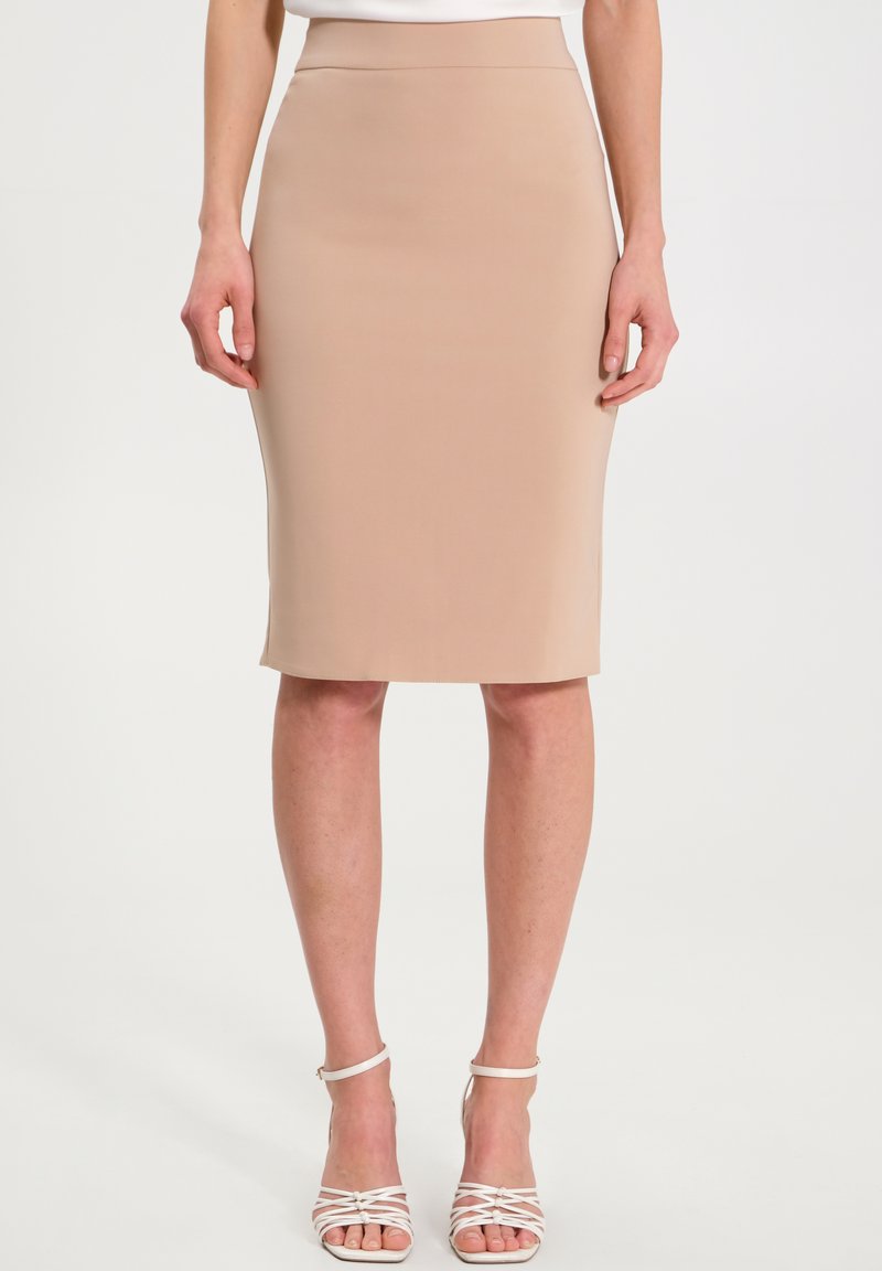 Beige Bleistiftrock aus glattem Stoff, hoher Taille und knielanger Schnitt, kombiniert mit weißen, schnürbaren High Heels.