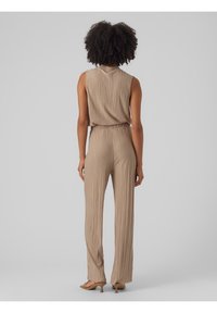 Beżowy kombinezon z plisowaniem, bez rękawów, elastycznym pasem i szerokimi nogawkami, charakteryzujący się gładką fakturą i subtelnym połyskiem.