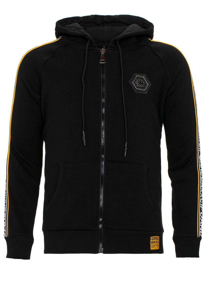 Schwarze Zip-Hoodie mit doppellagiger Kapuze, gelben Streifen an den Ärmeln, Fronttaschen und einem hexagonalen Logo-Patch auf der Brust.