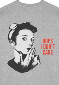 T-shirt grigia con un grafico in bianco e nero di una persona con un arco che fa il gesto di silenzio, accanto al testo "OOPS I DON'T CARE" in rosso.