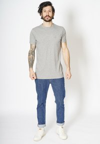 Grå bomulds T-shirt med korte ærmer, parret med opsmøgede blå denim jeans og hvide sneakers, præsenteret mod en neutral baggrund.