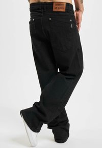 Schwarze Denim-Jeans mit lockerer Passform, fünf Taschen und einem Lederetikett am Bund. Saubere Nähte und subtile Designdetails.