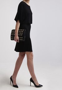 Černé šaty s krátkým rukávem a volným silueta, doplněné o černé lodičky na vysokém podpatku a černou kabelku s pozlacenými hřebíky.