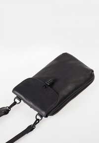 Borsa a tracolla in pelle nera con chiusura a zip e pattina con chiusura a scatto magnetico. Caratterizzata da una texture liscia e da una tracolla regolabile.