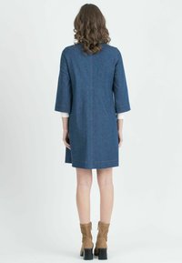 Denim mekko suoran leikkauksen, kolmanneksen hihasten, kontrastivärin ompeluiden ja keskikokoisen helmansa kanssa, jota on yhdistetty ruskeisiin nilkkasaappaisiin.