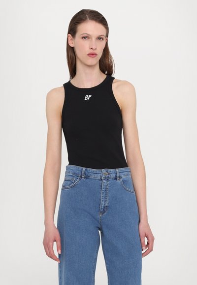 Black sleeveless tank top with round neckline, featuring a small white logo on the chest; paired with high-waisted blue jeans.