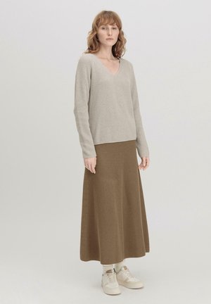 Lichtgrijze geribde gebreide trui met V-hals, gecombineerd met een bruine geribde maxi rok en crèmewitte sneakers, die een relaxte pasvorm toont.