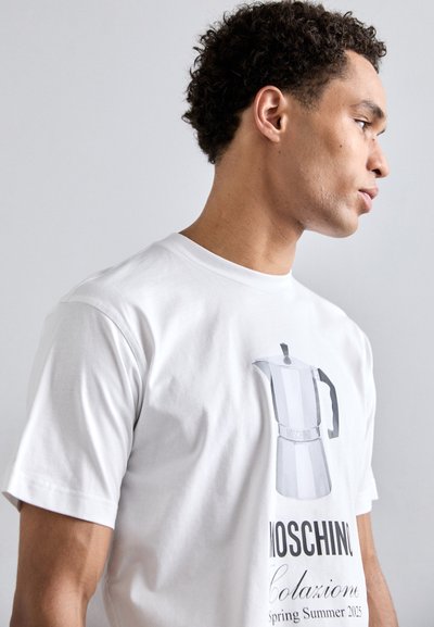 T-shirt en coton blanc avec un graphisme d'une cafetière moka, accompagné du texte "MOSCHINO Colazione Printemps Été 2023" en dessous du design.
