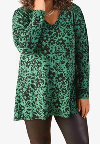 Green long-sleeve top with a V-neck, featuring a black floral pattern. Made of soft fabric, has a relaxed fit and falls just above the hips.