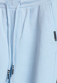 Light blue joggers made of textured fabric, featuring elastic waistband, drawstring with black and white stripes, and side pockets.