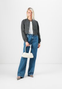 Gray cropped cardigan with button closure, white top, wide-leg blue jeans, and a small white handbag, paired with pointed beige shoes.
