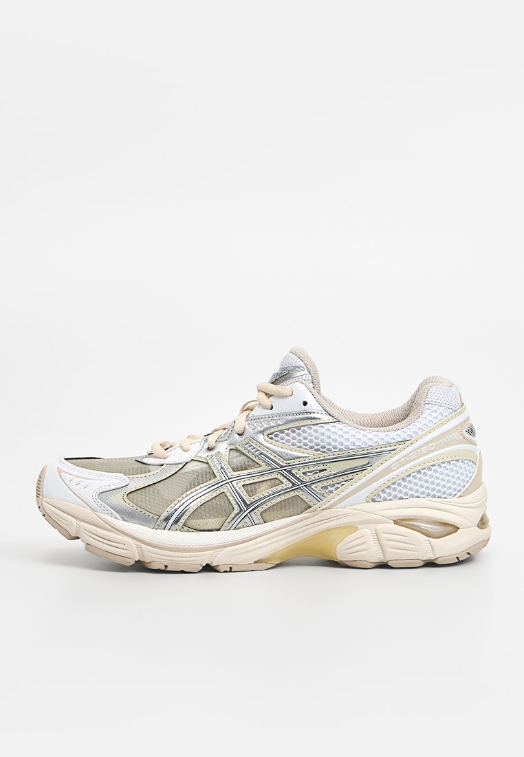 Hardloopschoen met een beige en wit mesh bovenkant, zilveren accenten en een comfortabele zool. Heeft een scherp ontwerp en vetersluiting.