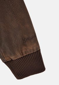 Bruine leren jas met een getextureerde mouw en een ribbelmanchet in donkerbruin. Subtiele merkdetail. Het oppervlak vertoont fijne kreuken en nerfpatronen.
