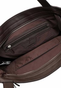 Interieur van een bruine leren handtas met een ritsvak, een schuifvak en een zachte voering. Stiksel langs de randen zichtbaar.