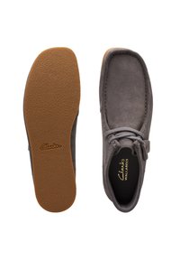 Zapato de ante gris con cordones y punta redonda, que presenta una suela de goma marrón claro y sutiles acentos de costura a lo largo del borde. Marca Clarks en el interior.