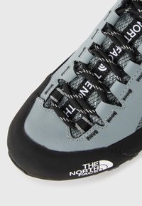 Gray and black climbing shoe featuring a textured upper, reinforced toe cap, and distinctive lace design with branding on the side.